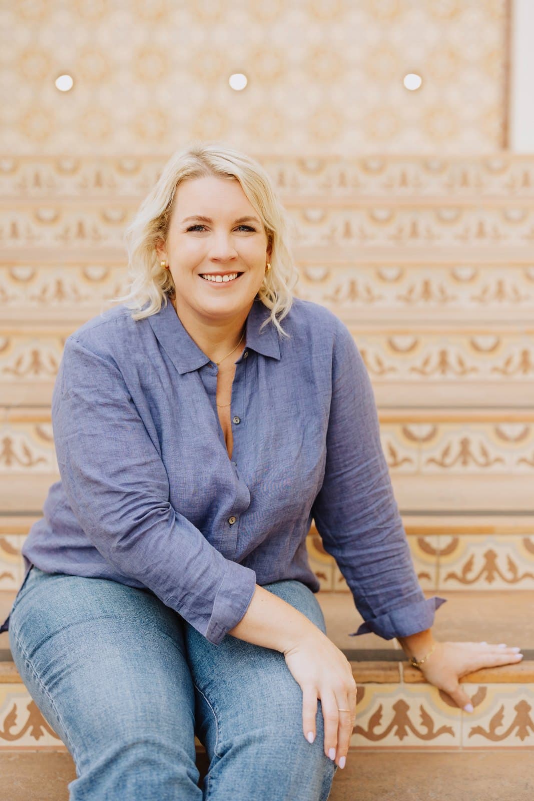 Jessica Burns seated on tiled steps in a blue linen shirt